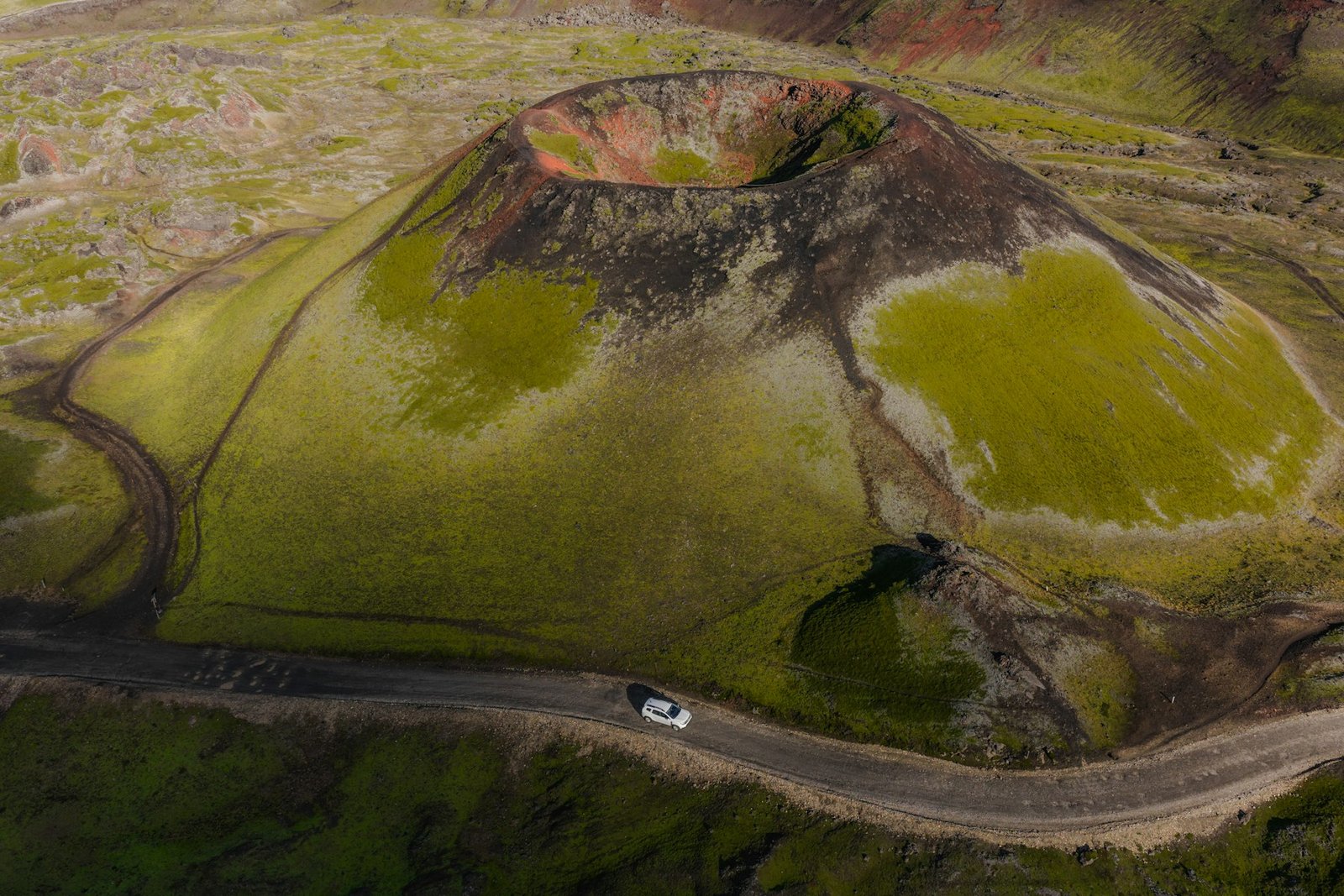 A car on a gravel track beside a volcanic crater in the Icelandic highlands