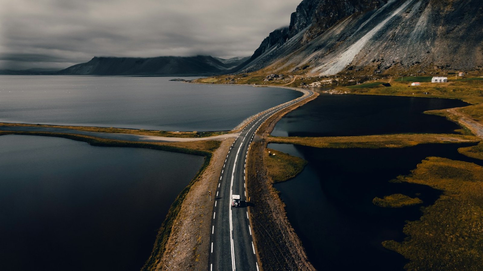 Empty road leading towards dark, snow-streaked mountains in Iceland
